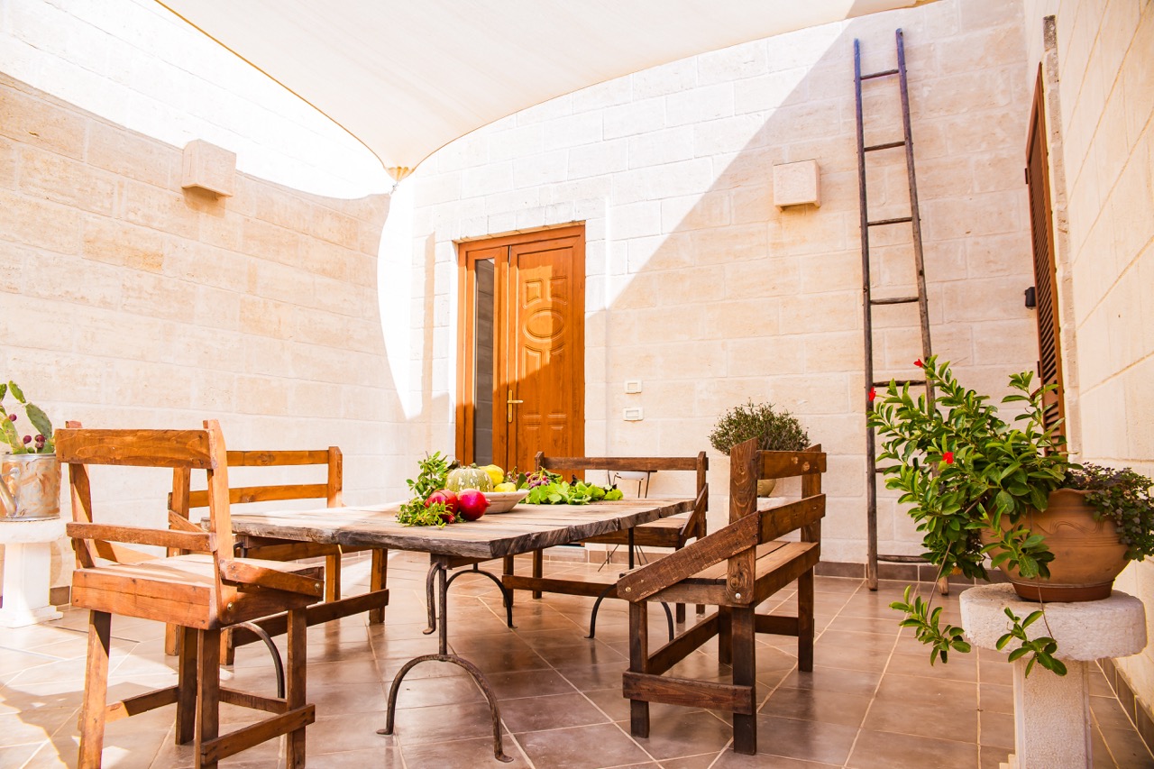 Patio con tavolo e sedie in legno, frutta sul tavolo e piante in vaso.