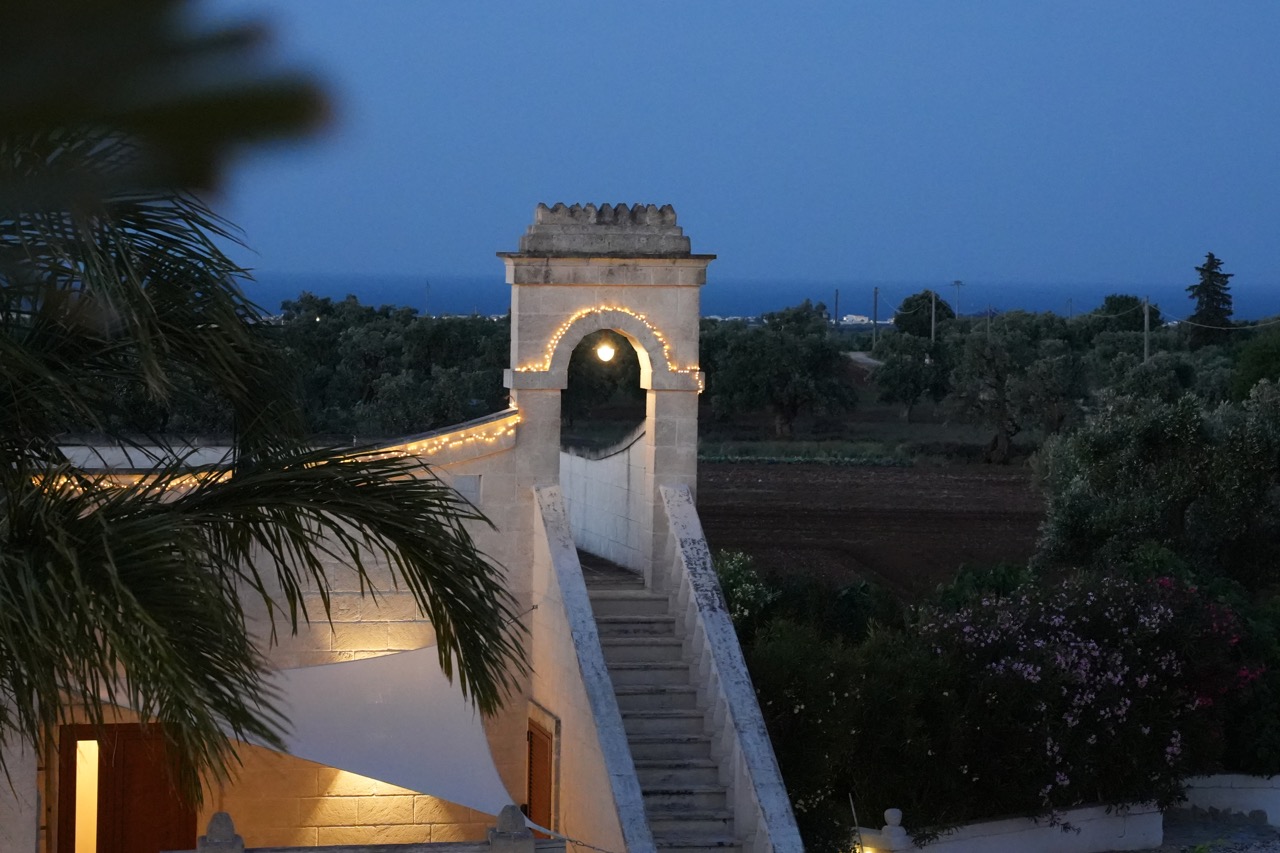 Scala in pietra e arco illuminato con la campagna sullo sfondo al crepuscolo.