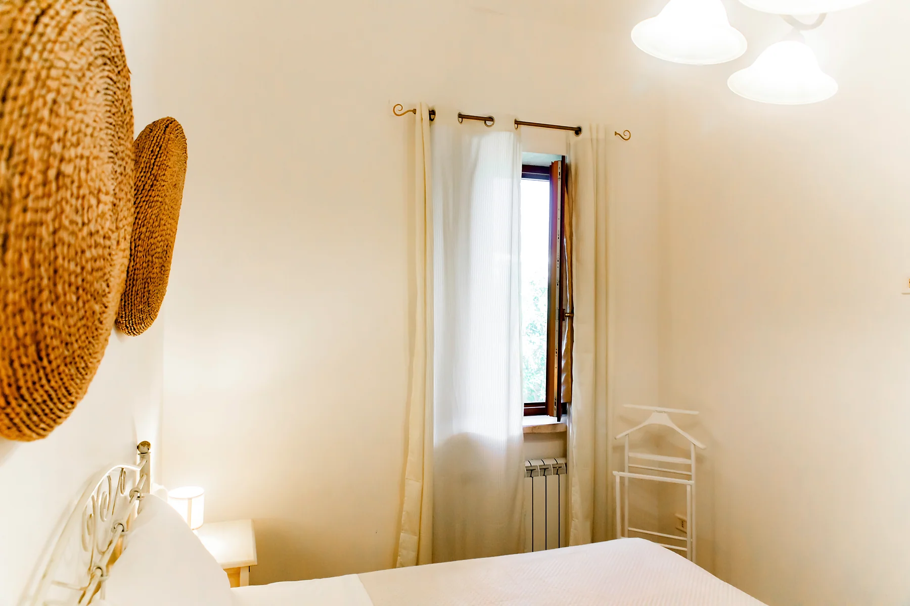 Camera luminosa con letto bianco e decorazioni intrecciate alla parete